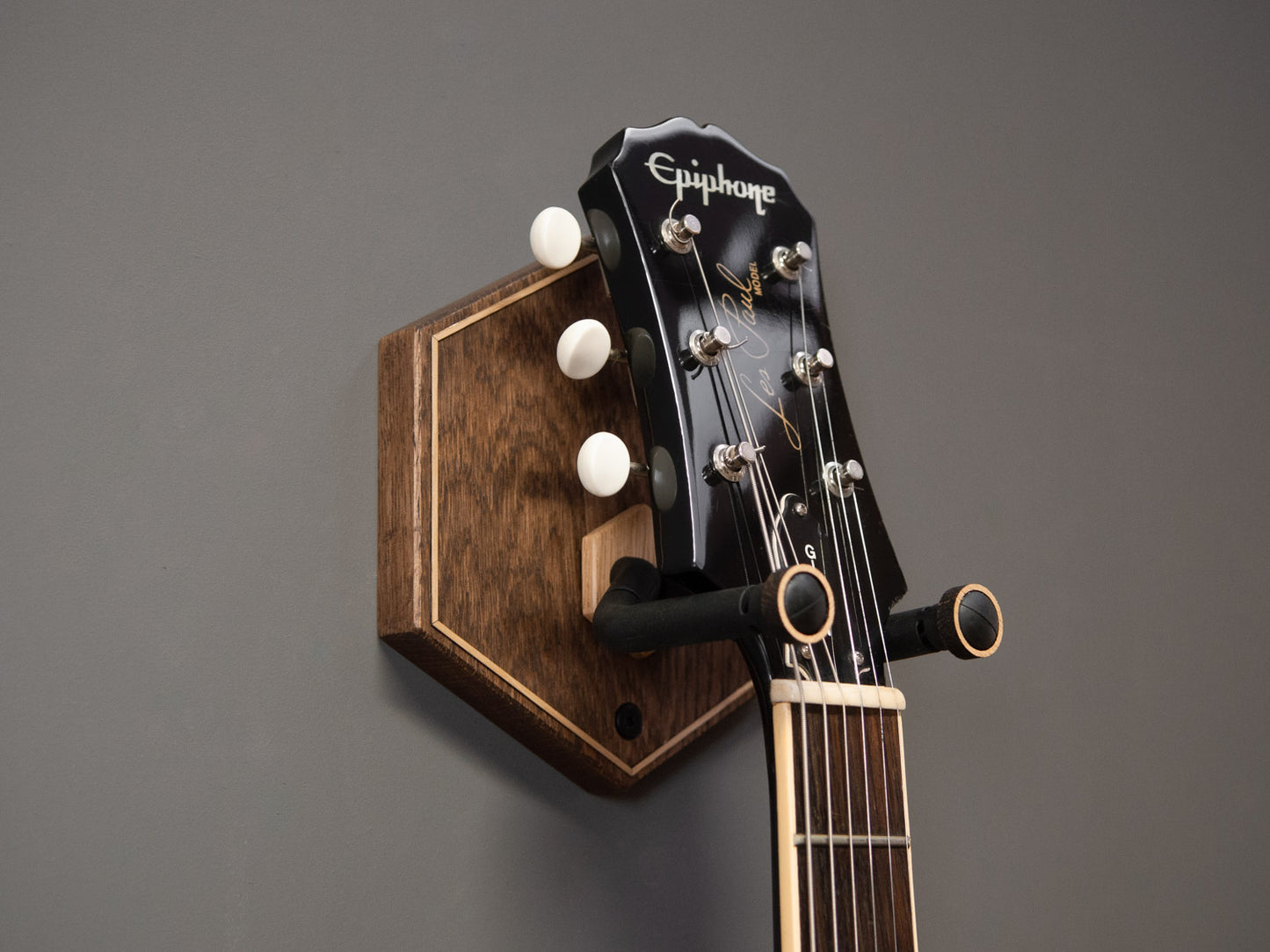 A black guitar hung on a dark wooden guitar wall mount