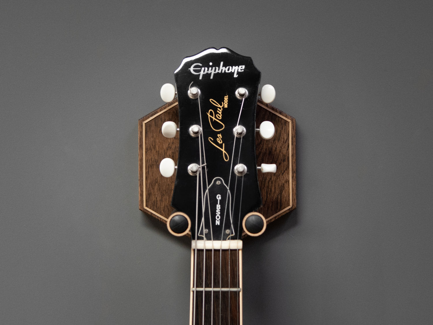 Front view of a guitar neck, hung on a dark oak wall mount, with light oak details