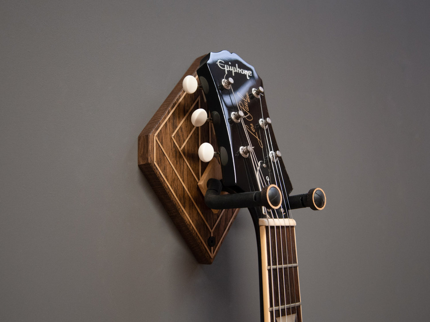 A black guitar hung on a dark wooden guitar wall mount