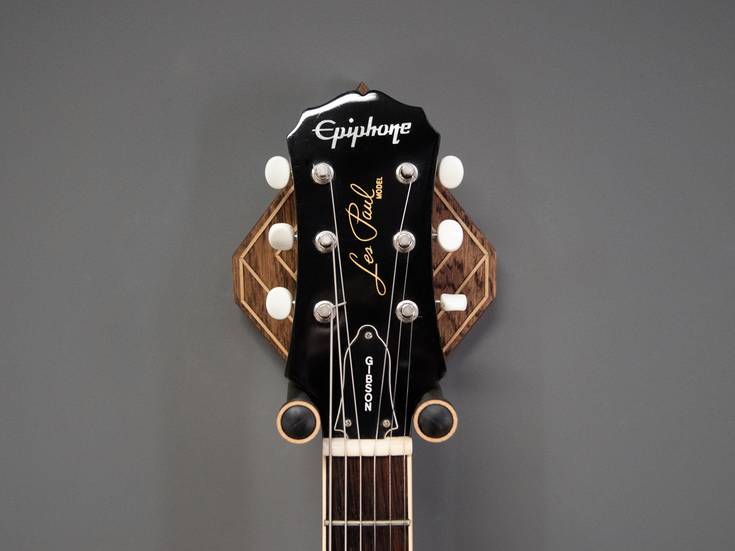 Front view of a guitar neck, hung on a dark oak wall mount, with light oak details