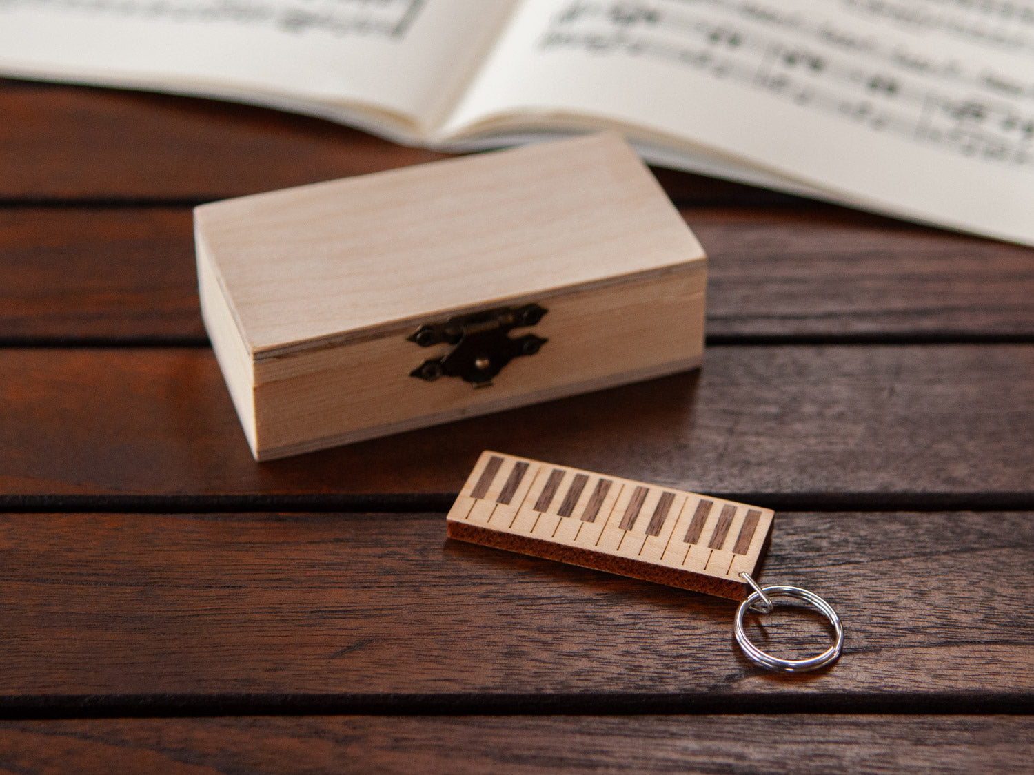 A piano keychain positioned in front of a small wooden box.