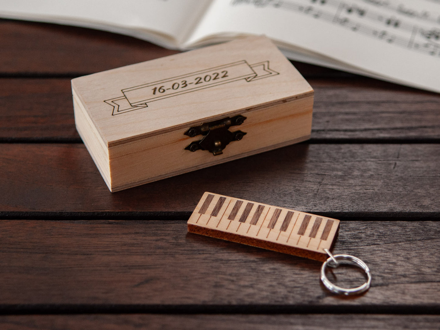 A keychain shaped like a piano in front of a small engraved wooden box.