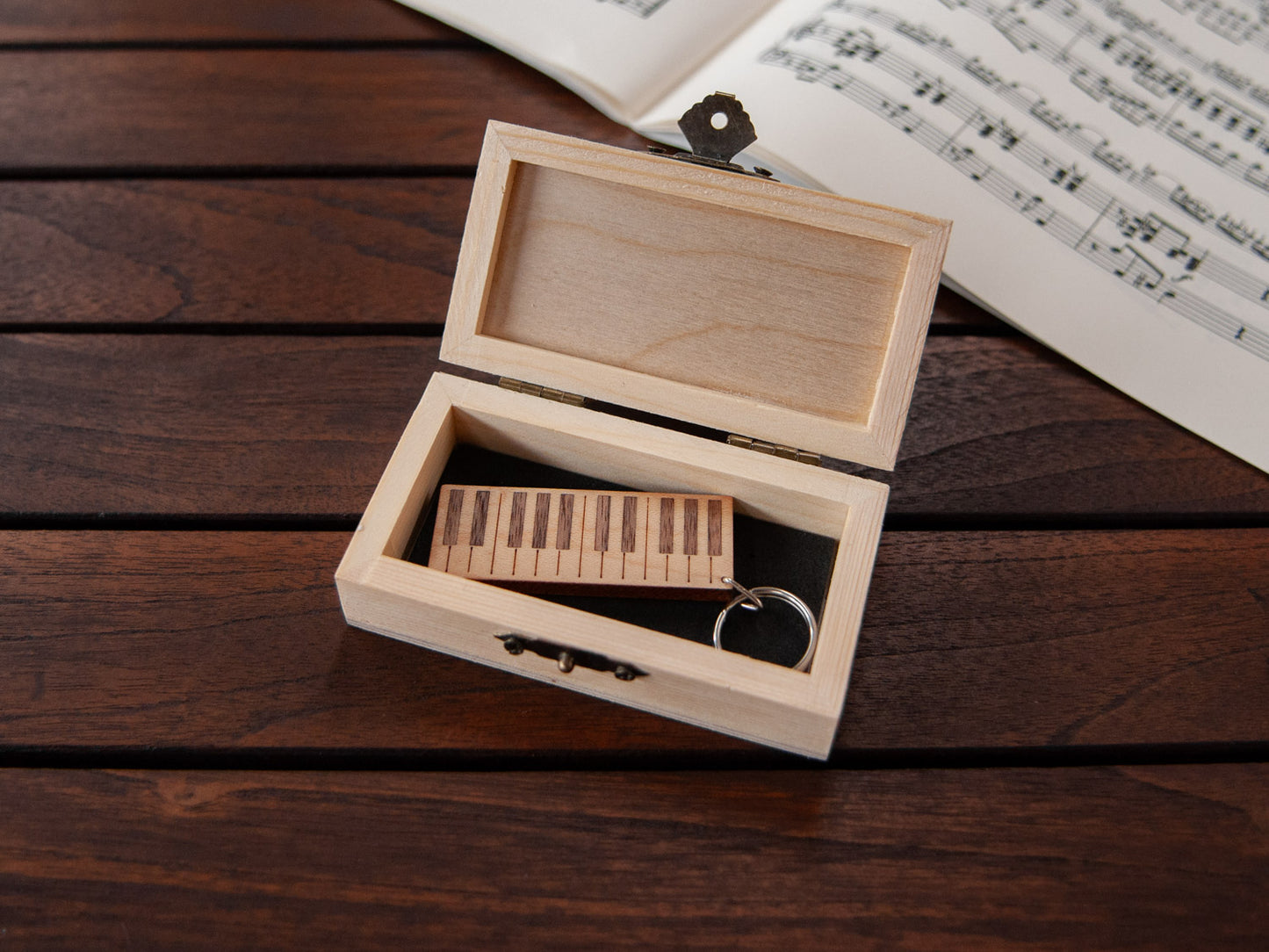 A piano shaped keychain placed inside a compact wooden box