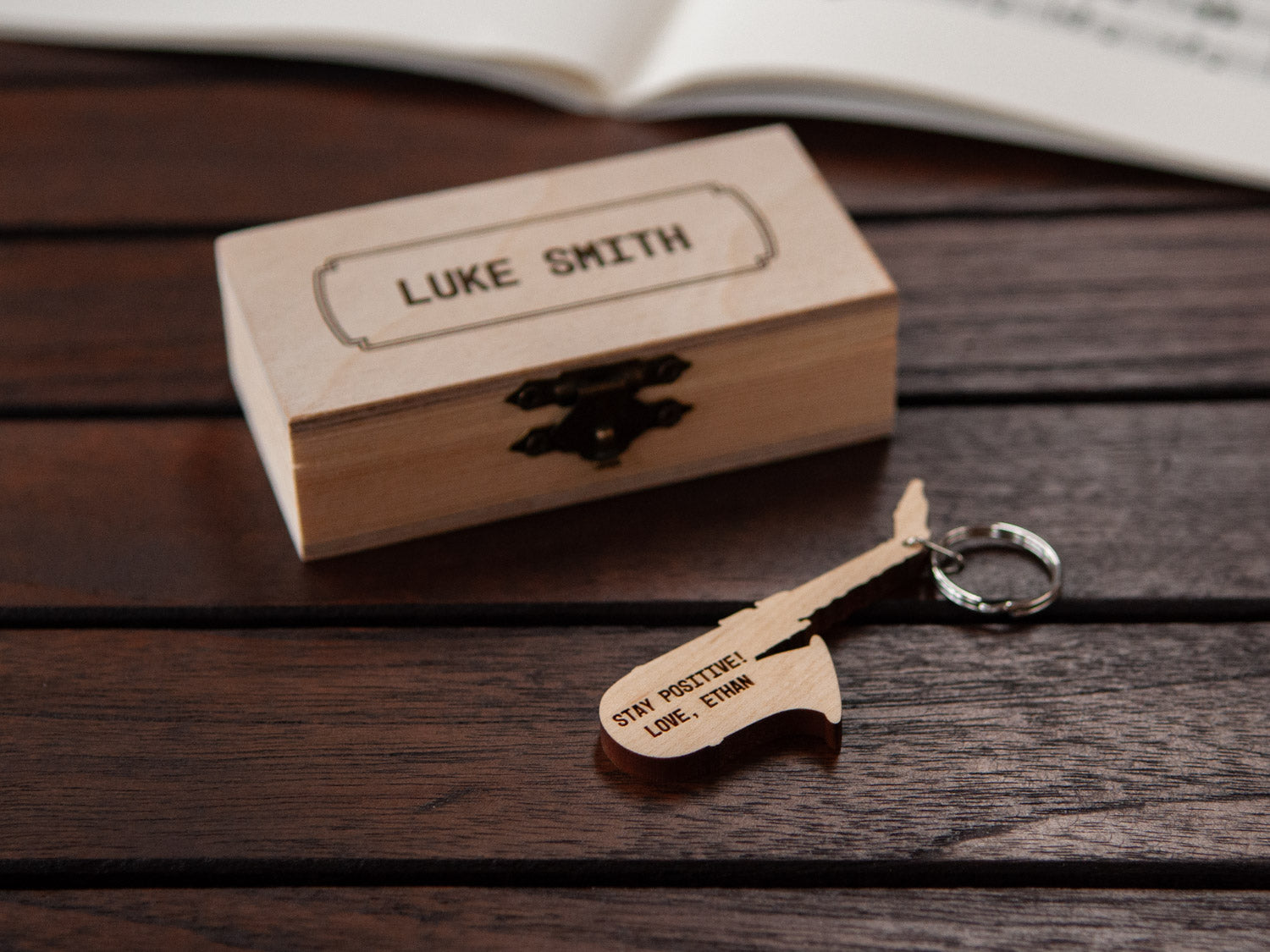 Saxophone keychain displayed in front of a small wooden box, with a custom engraving.