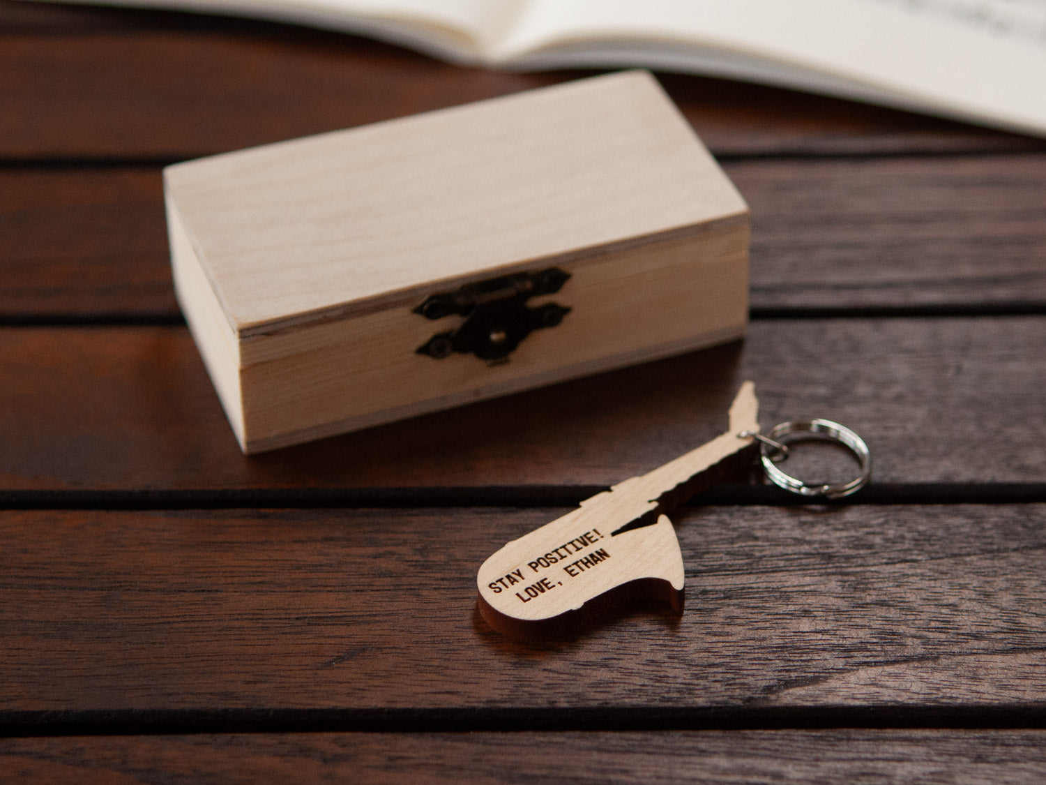 An engraved saxophone keychain positioned in front of a small wooden box.