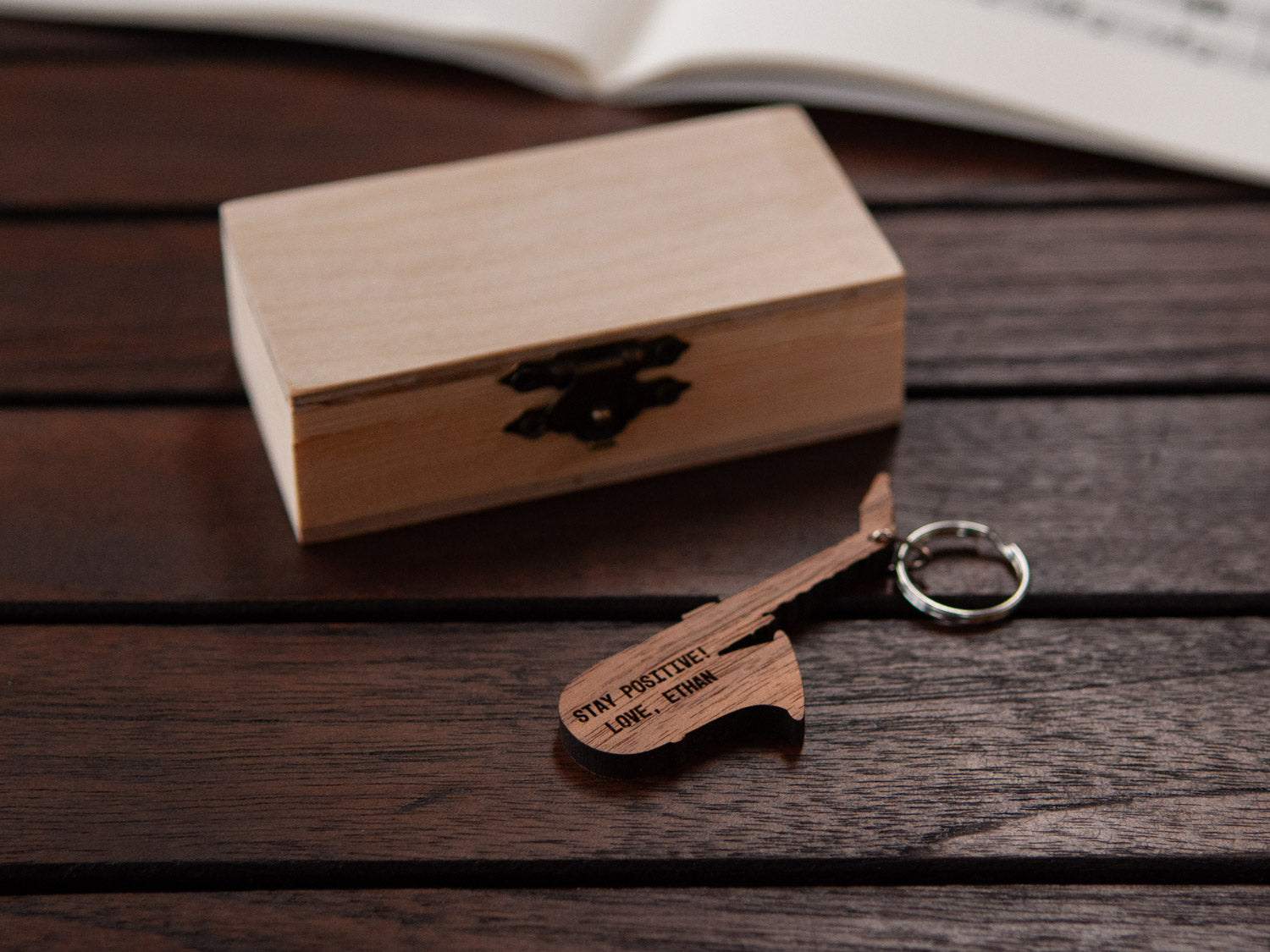 An engraved saxophone keychain positioned in front of a small wooden box.