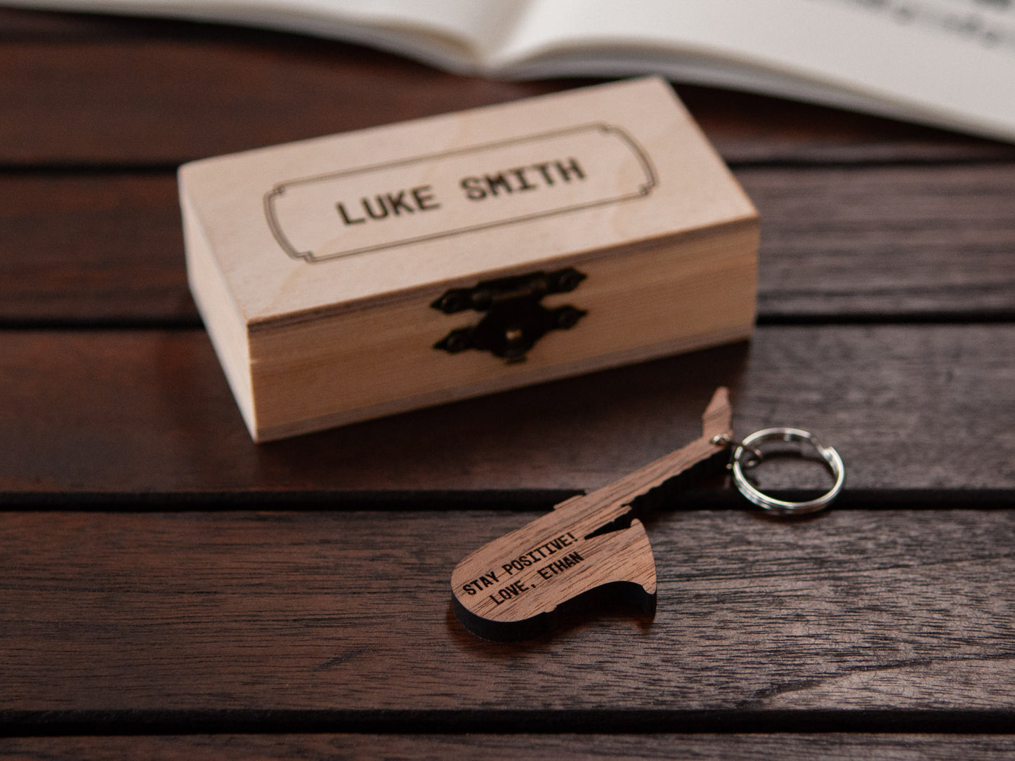 Saxophone keychain displayed in front of a small wooden box, both with a custom engraving.