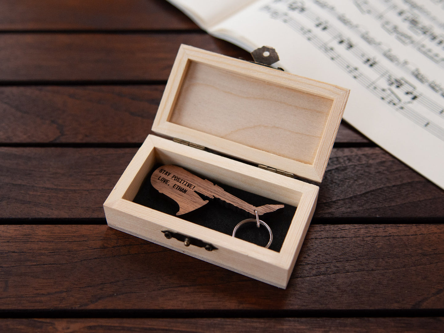 A saxophone shaped keychain placed inside a compact wooden box, featuring a custom engraving.