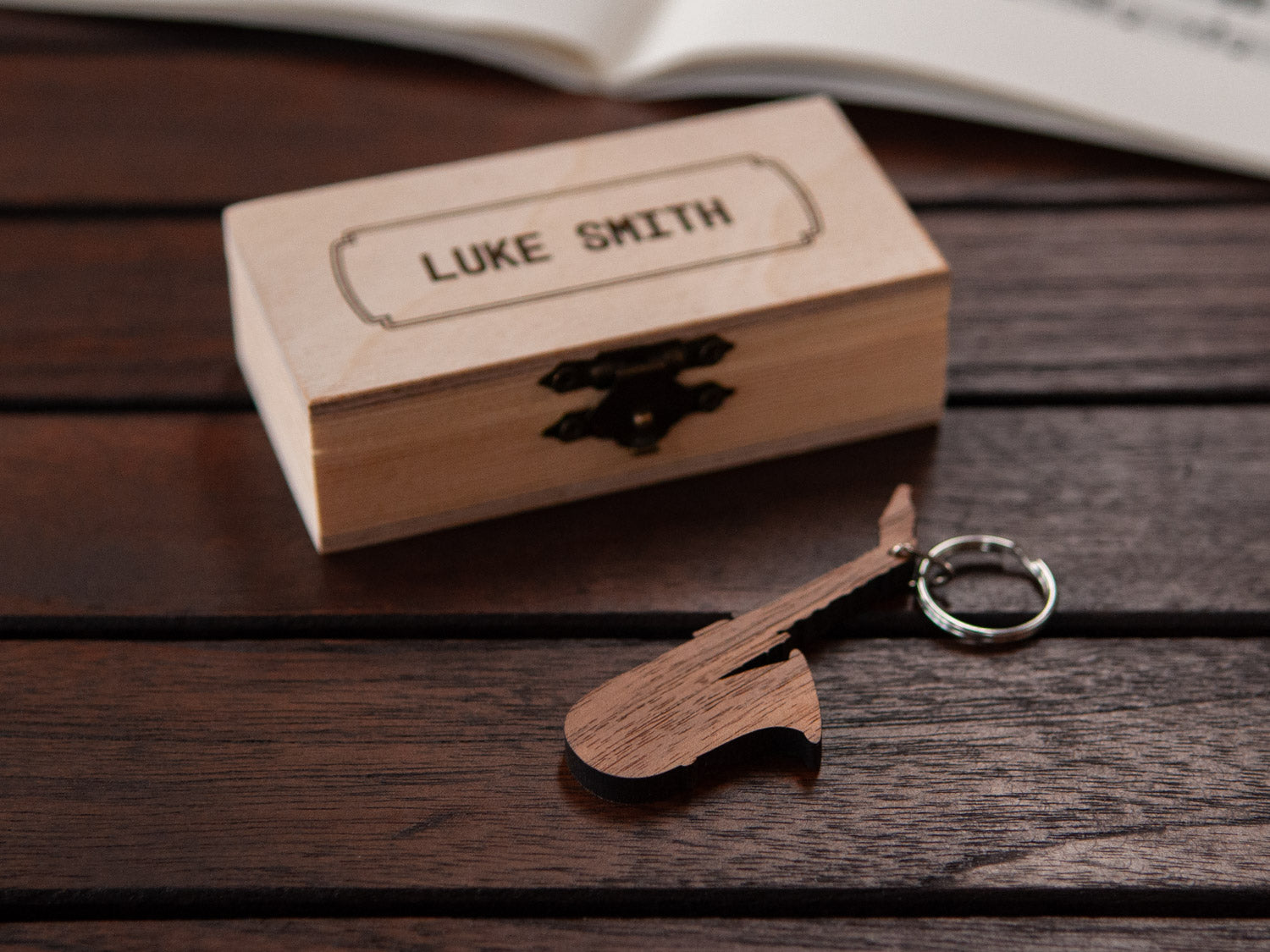 A keychain shaped like a saxophone in front of a small engraved wooden box.