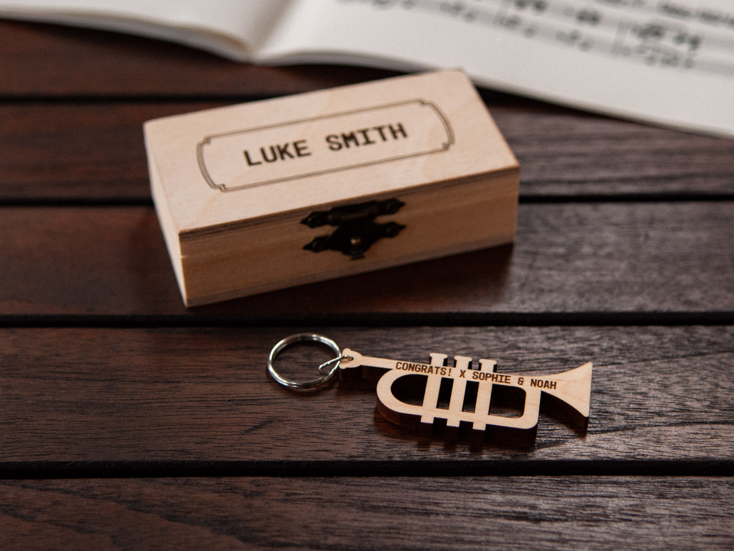 Trumpet keychain displayed in front of a small wooden box, both with a custom engraving.