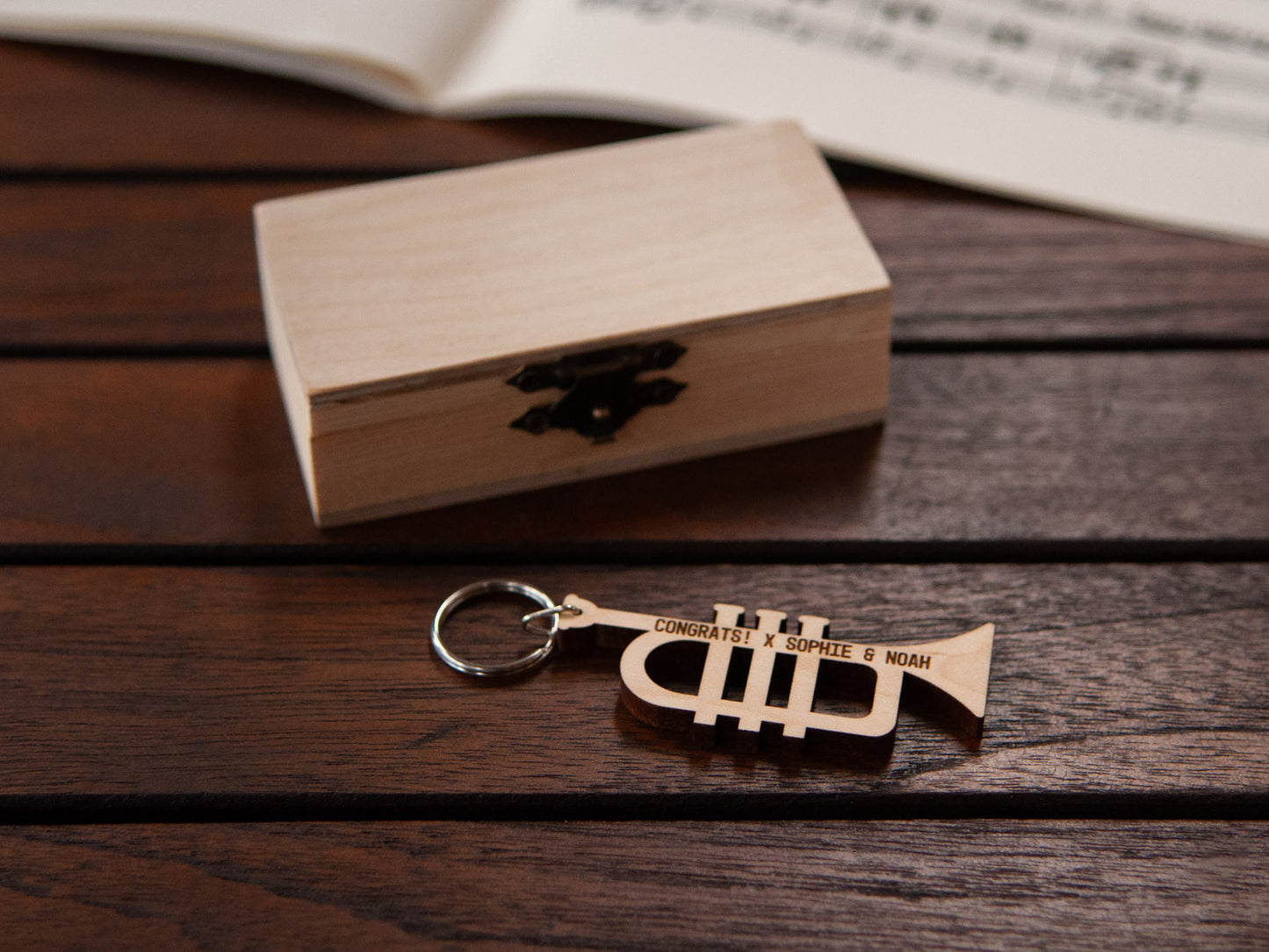 An engraved trumpet keychain positioned in front of a small wooden box.