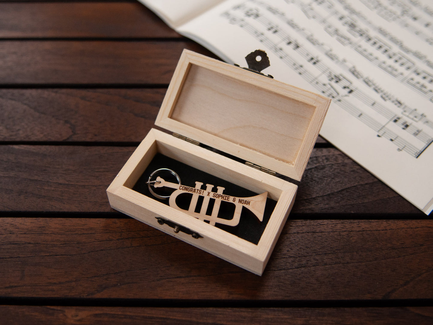 A trumpet shaped keychain placed inside a compact wooden box, featuring a custom engraving.