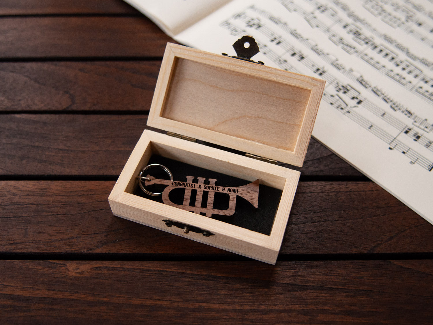 A trumpet shaped keychain placed inside a compact wooden box, featuring a custom engraving.