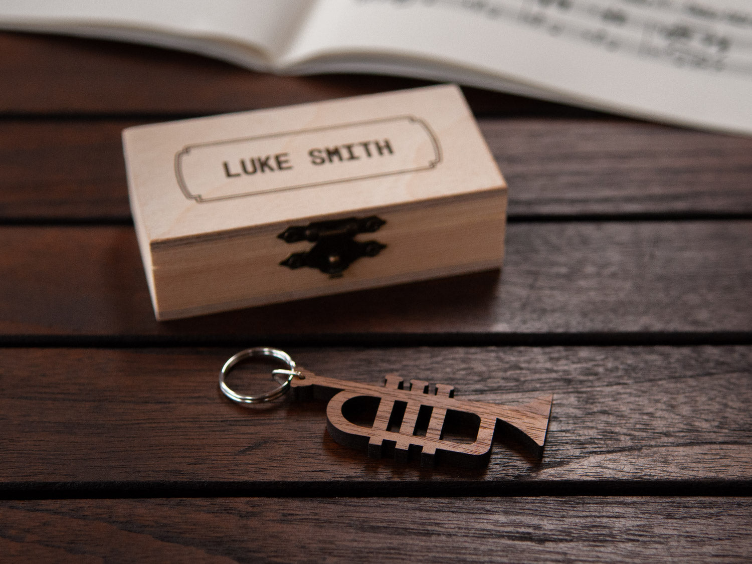 A keychain shaped like a trumpet in front of a small engraved wooden box.