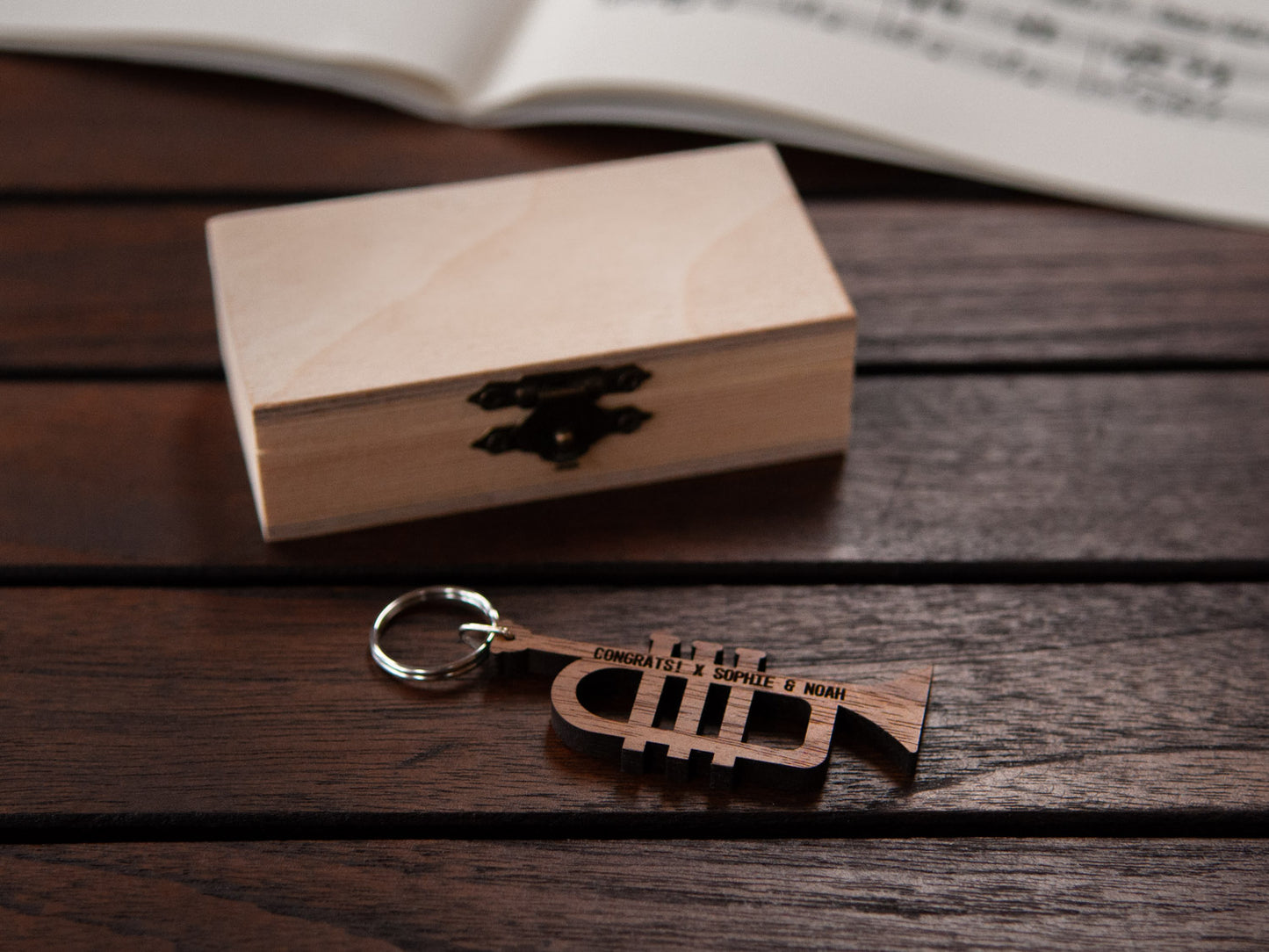 An engraved trumpet keychain positioned in front of a small wooden box.