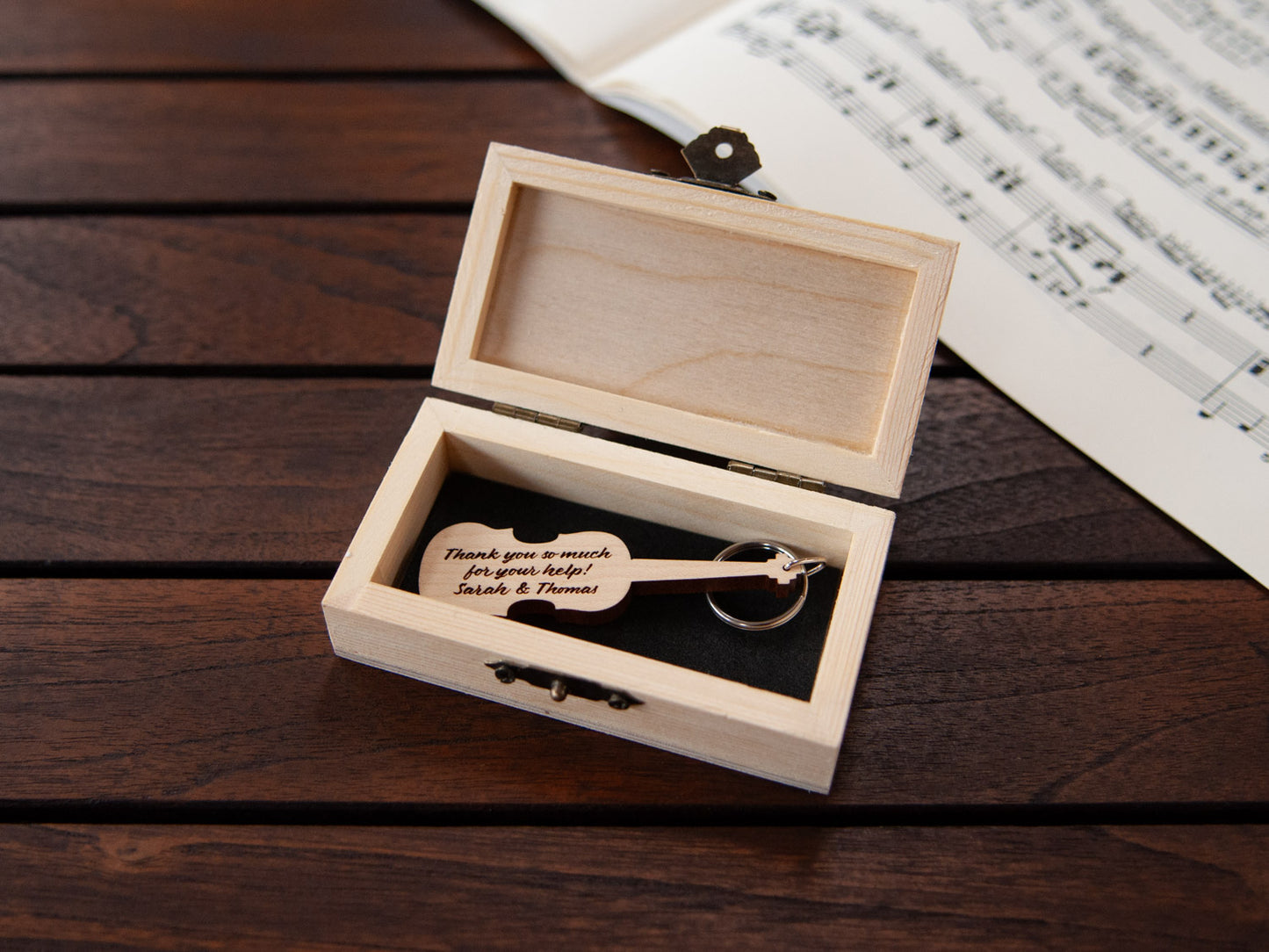 A violin shaped keychain placed inside a compact wooden box, featuring a custom engraving.