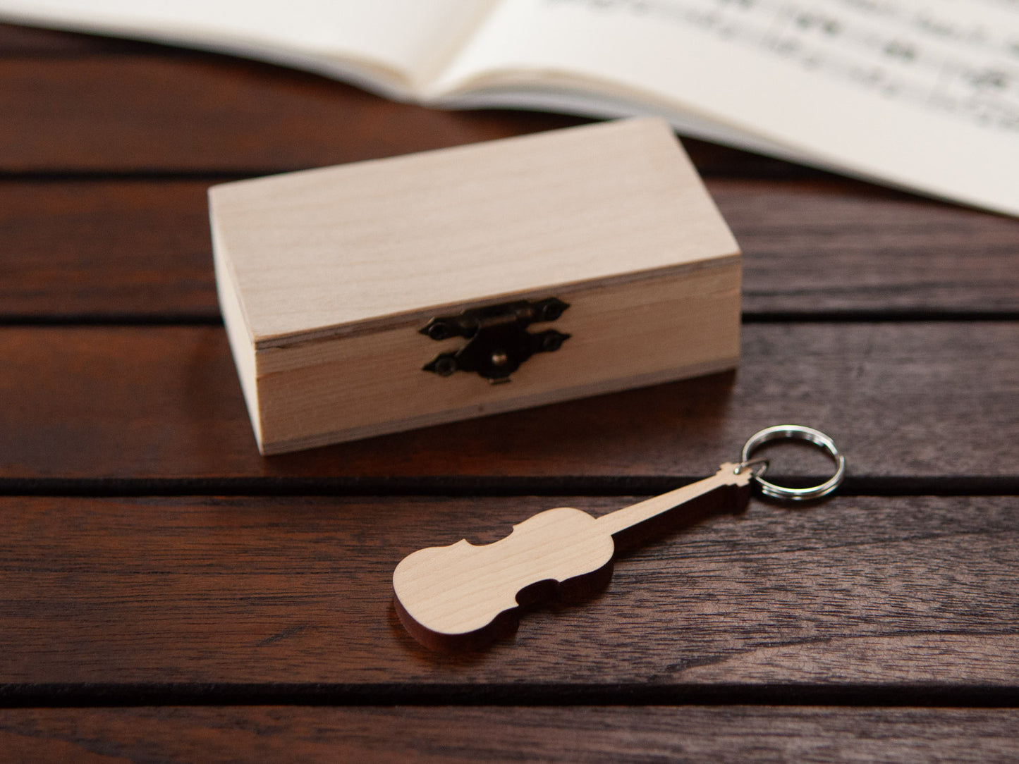 A violin keychain positioned in front of a small wooden box.