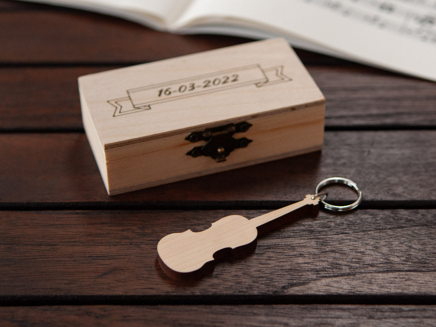 A keychain shaped like a violin in front of a small engraved wooden box.