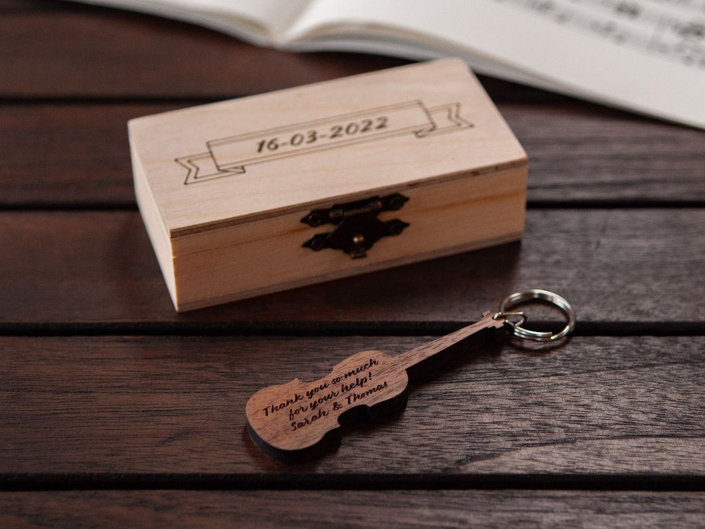 Violin keychain displayed in front of a small wooden box, both with a custom engraving.