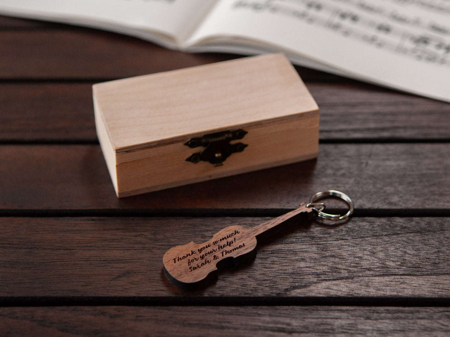 An engraved violin keychain positioned in front of a small wooden box.