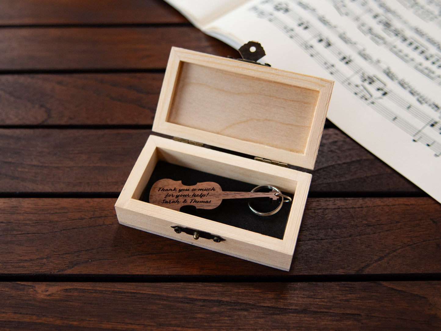 A violin shaped keychain placed inside a compact wooden box, featuring a custom engraving.