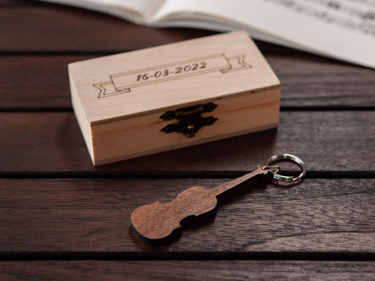 A keychain shaped like a violin in front of a small engraved wooden box.