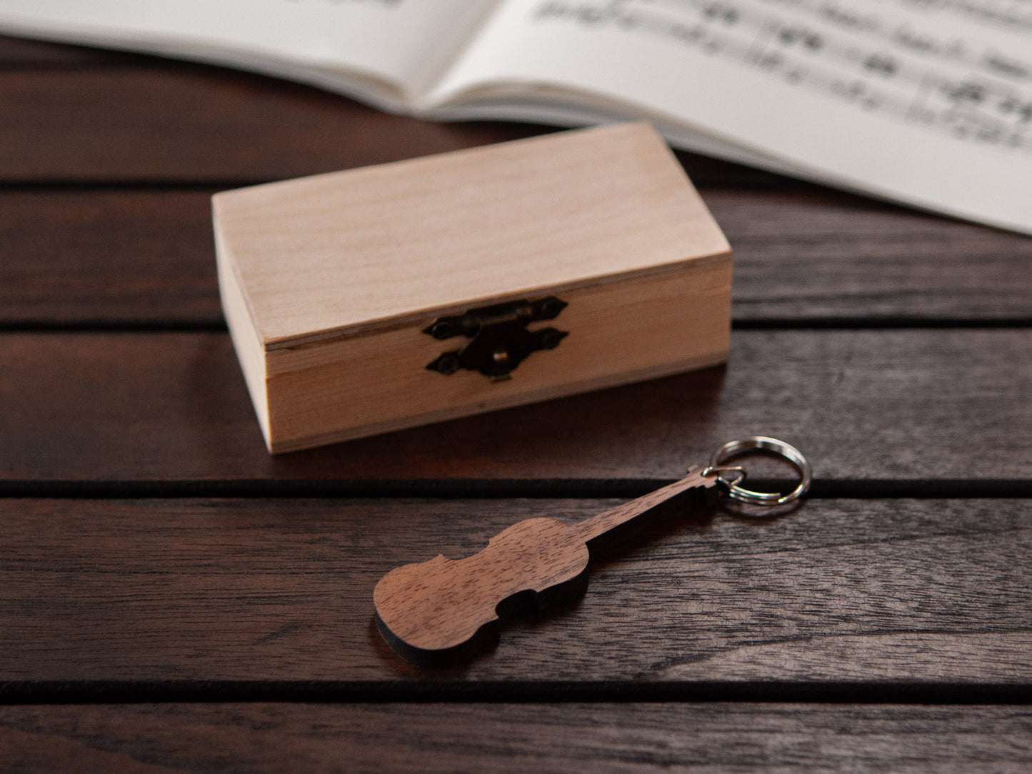 A violin keychain positioned in front of a small wooden box.